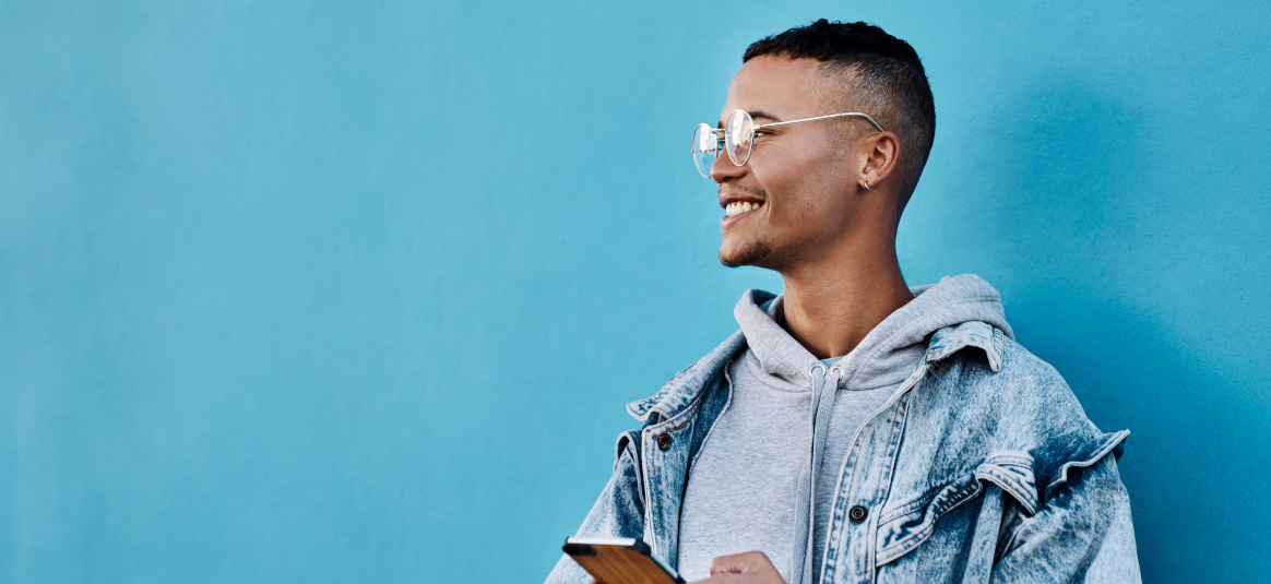 Photo of a smiling man holding a phone in front of a blue background