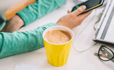 Photo of a coffee cup, laptop and pair of hands