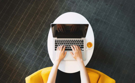 Photo of an open laptop, coffee cup and pair of hands