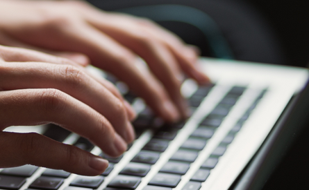 Photo of two hands typing on an open laptop