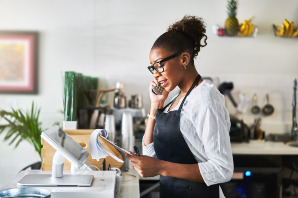 Photo of a woman with apron speaking on a phone in front of a till